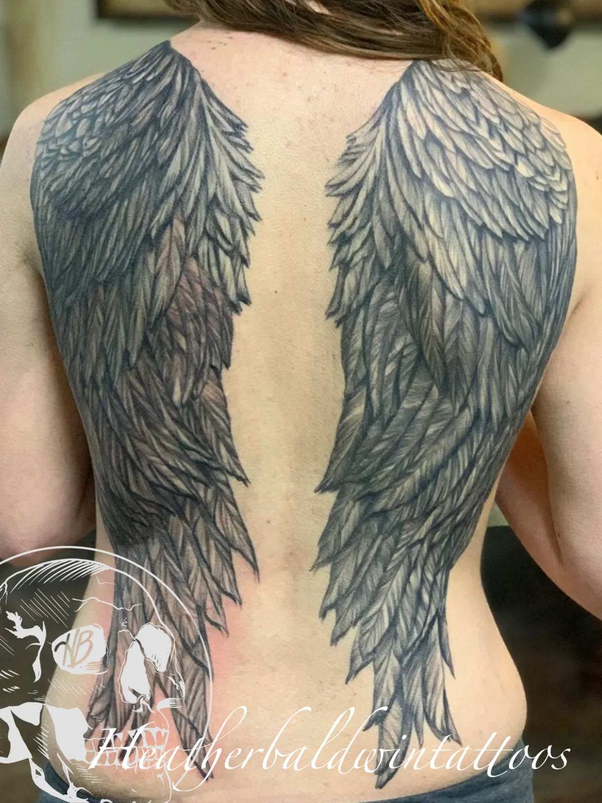 Angel wing tattoo by Heather Baldwin — full feathered wings spanning the entire back in detailed black and grey realism
