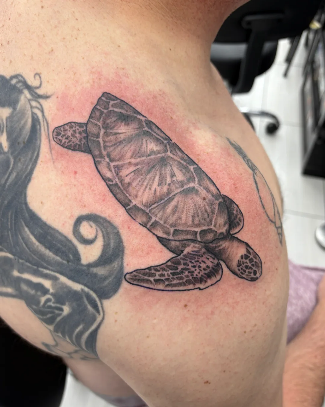 Honu tattoo by Heather Baldwin — Hawaiian green sea turtle in detailed black and grey realism, shoulder placement next to existing pieces