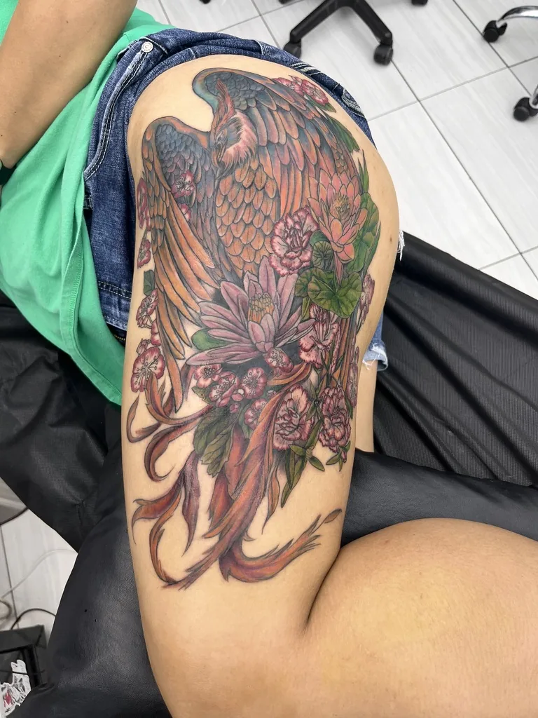 Phoenix tattoo by Heather Baldwin — large mythological phoenix in autumn oranges with cherry blossoms and lotus flowers wrapping the hip and thigh