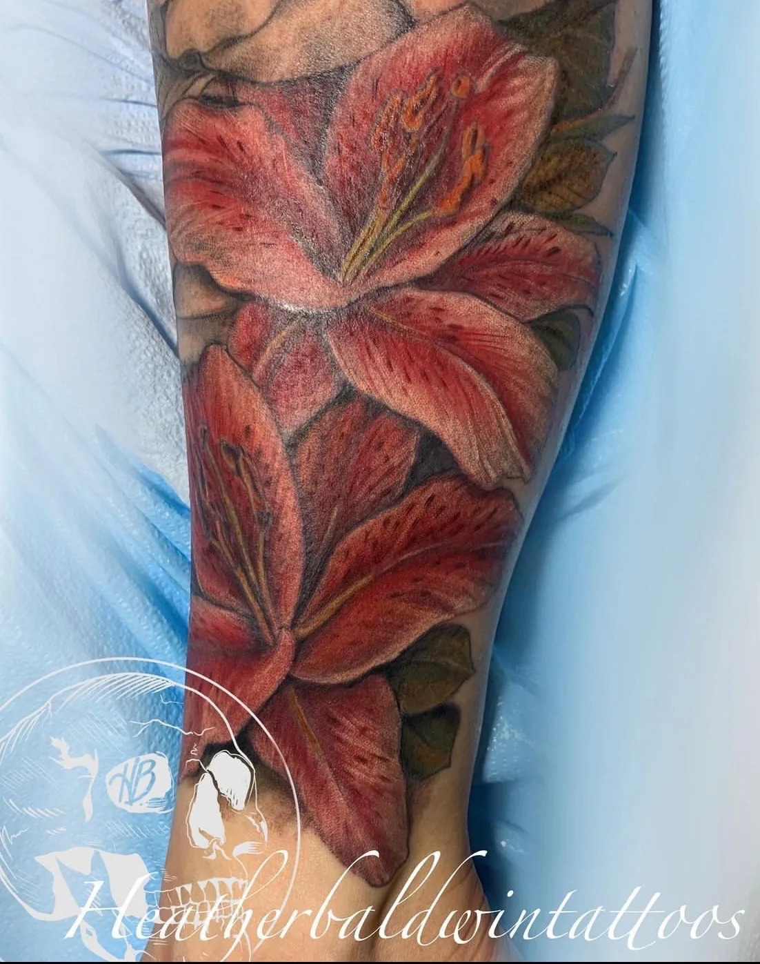 Floral tattoo by Heather Baldwin — two large pink stargazer lilies in soft color realism wrapping the forearm