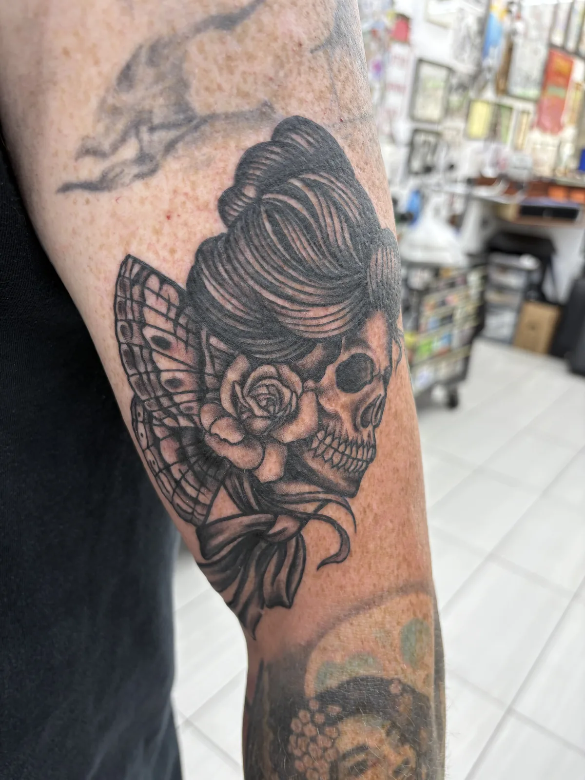 Neo-traditional tattoo by Heather Baldwin — woman with skull face holding a rose, lace fan and pearls framing the design, forearm placement