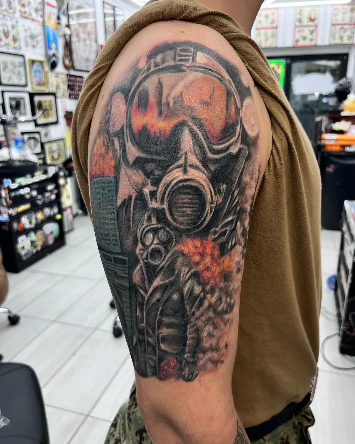 Realism tattoo by Heather Baldwin — soldier in a gas mask reflecting a burning city in the visor, fully saturated color realism on the upper arm