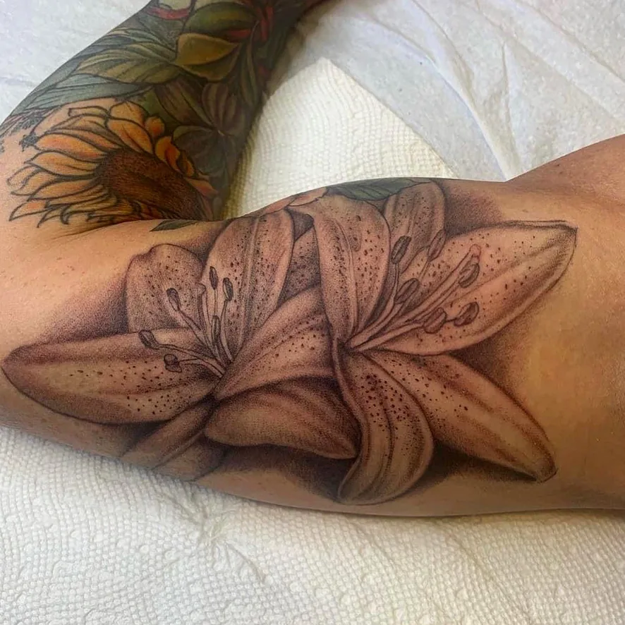 Floral tattoo by Heather Baldwin — two stargazer lilies in soft black and grey dotwork on the inner bicep