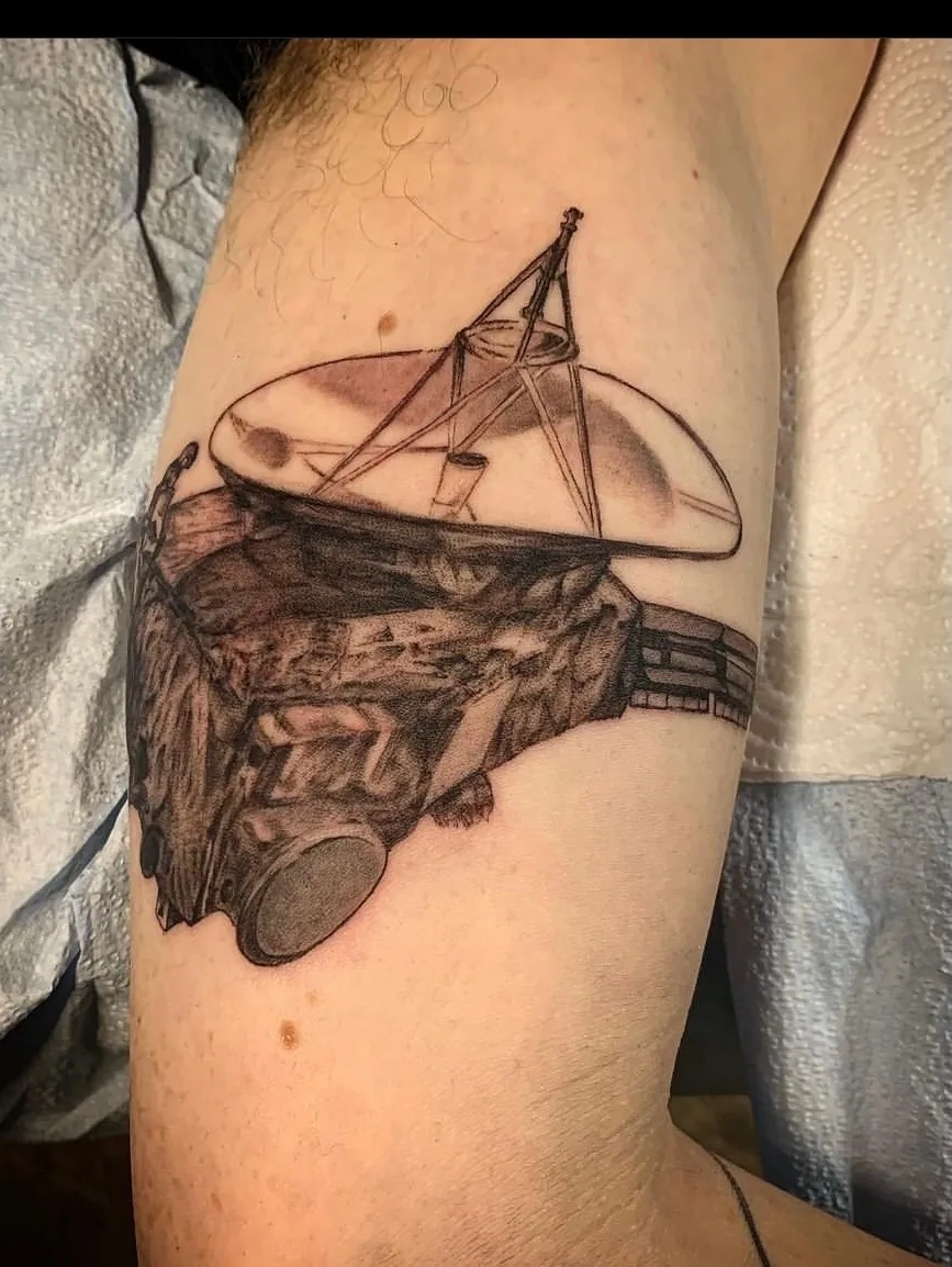 Voyager satellite tattoo by Heather Baldwin — NASA deep-space probe rising over an asteroid in detailed black and grey realism on the bicep